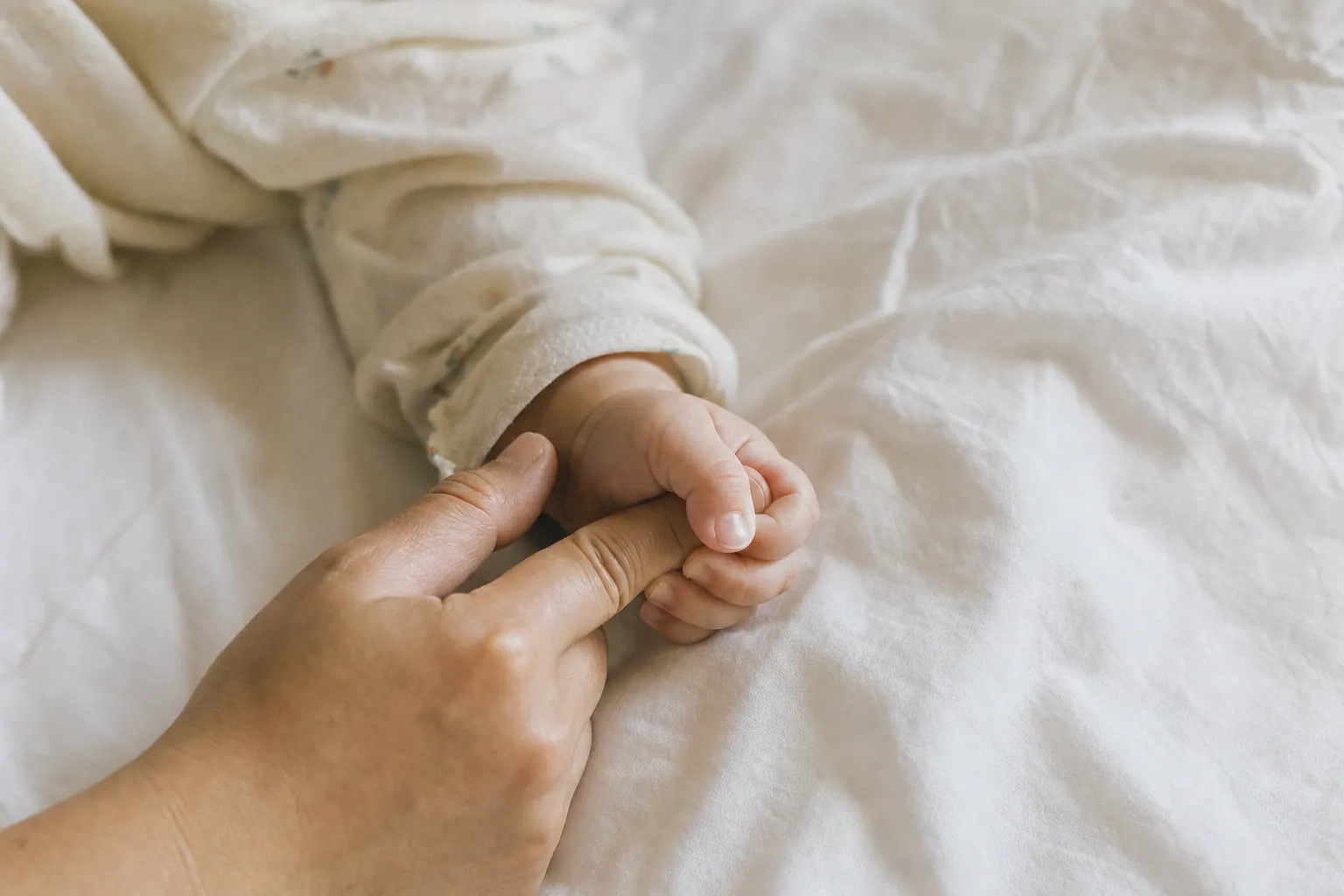 A baby's hand wrapped around an adult's finger